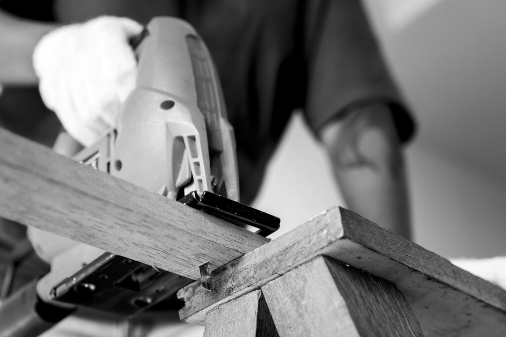 Persona utilizando una sierra eléctrica para cortar una tabla de madera en un banco de trabajo, en blanco y negro