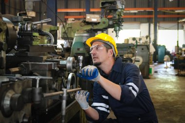 Trabajador industrial con casco y gafas de seguridad operando una máquina en una fábrica, concentrado en labores de mantenimiento o ajuste técnico