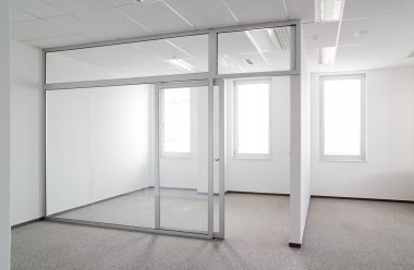 Espacio de oficina moderno y vacío con paredes blancas, suelo alfombrado y división interior de cristal.