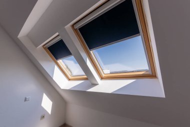 Ventanas de techo inclinadas con persianas enrollables negras, dejando entrar luz natural.