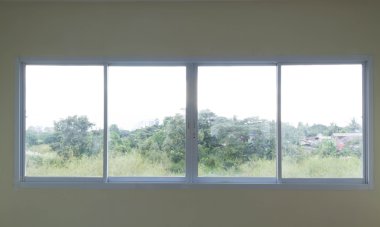 Ventana corrediza de aluminio blanco con cuatro paneles que ofrece una vista despejada a una zona verde con árboles.