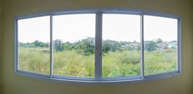 Amplia ventana de aluminio con cuatro hojas correderas y vista a un campo verde con árboles.